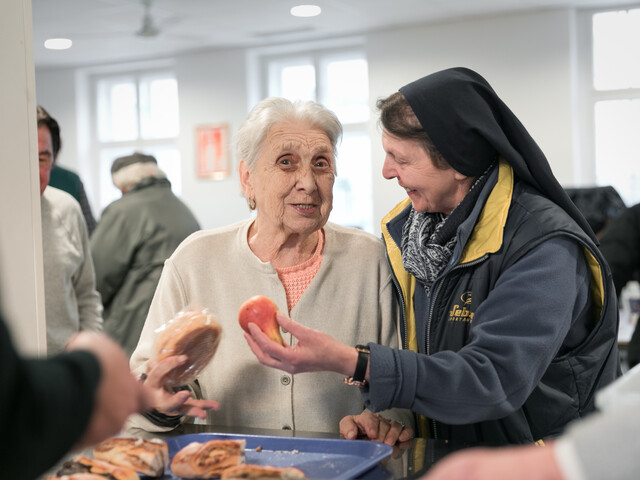 Eine ältere Frau bekommt bei der Essensausgabe im Marienstüberl einen Apfel