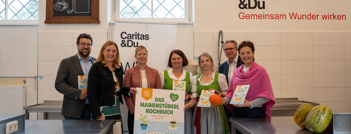 Gruppenfoto von Menschen, die das Marienstüberl-Kochbuch halten. 