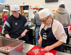 Ein Koch und eine Köchin schneiden Schinken. 