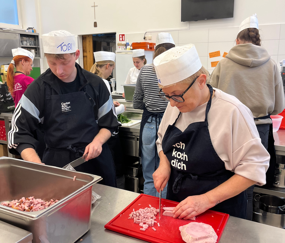 Ein Koch und eine Köchin schneiden Schinken. 